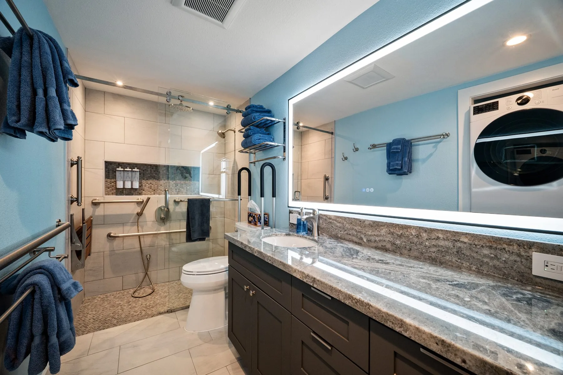 Bathroom vanity with lit mirror, grab bars, and walk-in shower