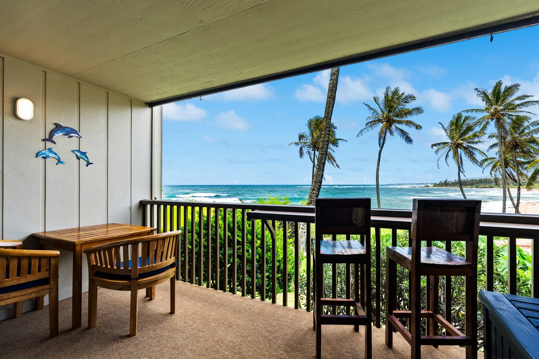 Covered oceanfront lanai with teak seating and palm-framed ocean view at Wailua Bay View #102